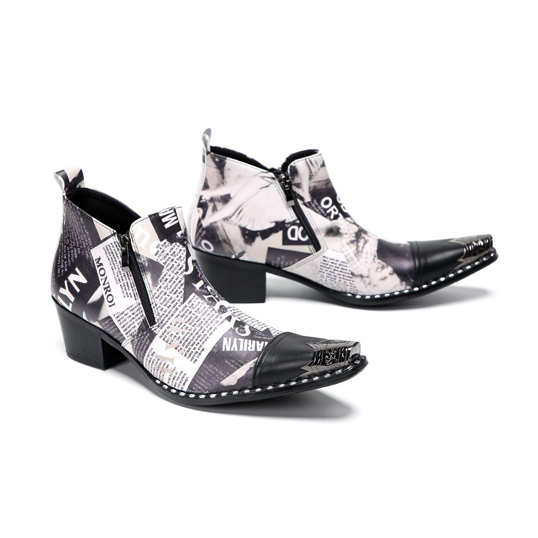 A pair of men's black and white newspaper print ankle boots with a pointed metal toe, side zipper, and block heel.