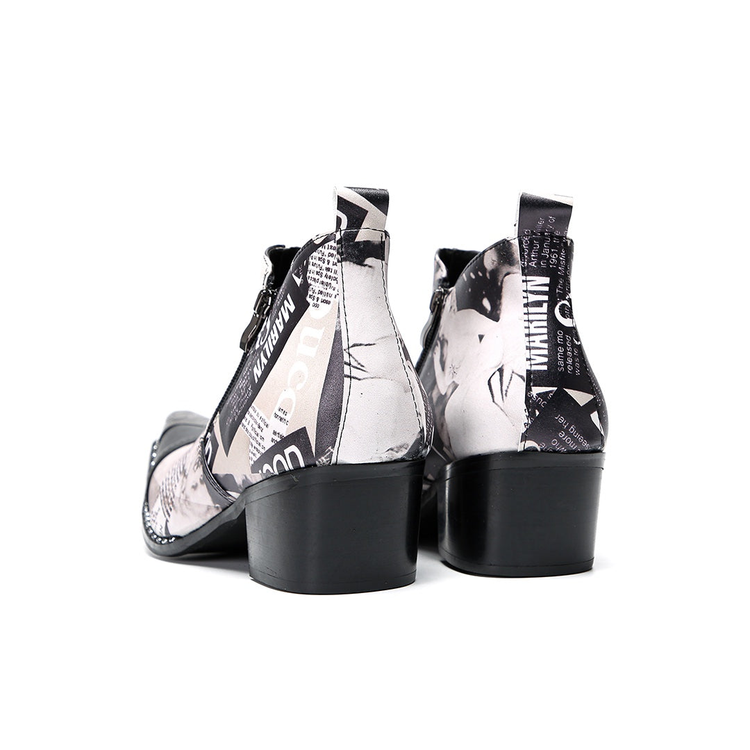 A pair of men's black and white newspaper print ankle boots with a pointed metal toe, side zipper, and block heel.