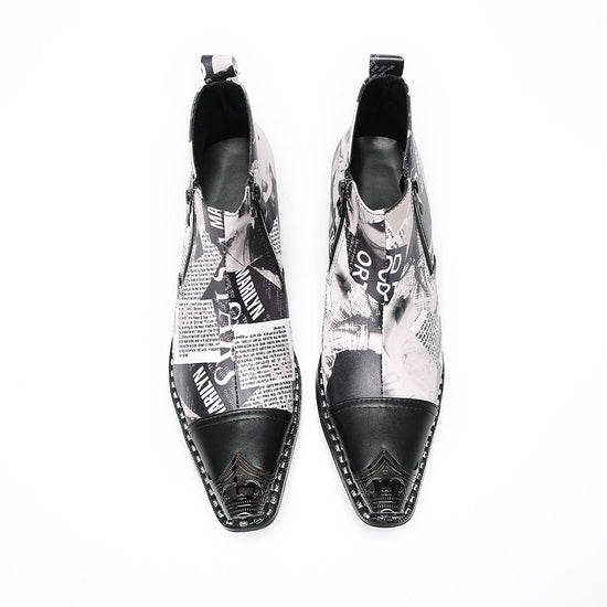 A pair of men's black and white newspaper print ankle boots with a pointed metal toe, side zipper, and block heel.