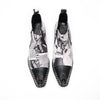 A pair of men's black and white newspaper print ankle boots with a pointed metal toe, side zipper, and block heel.