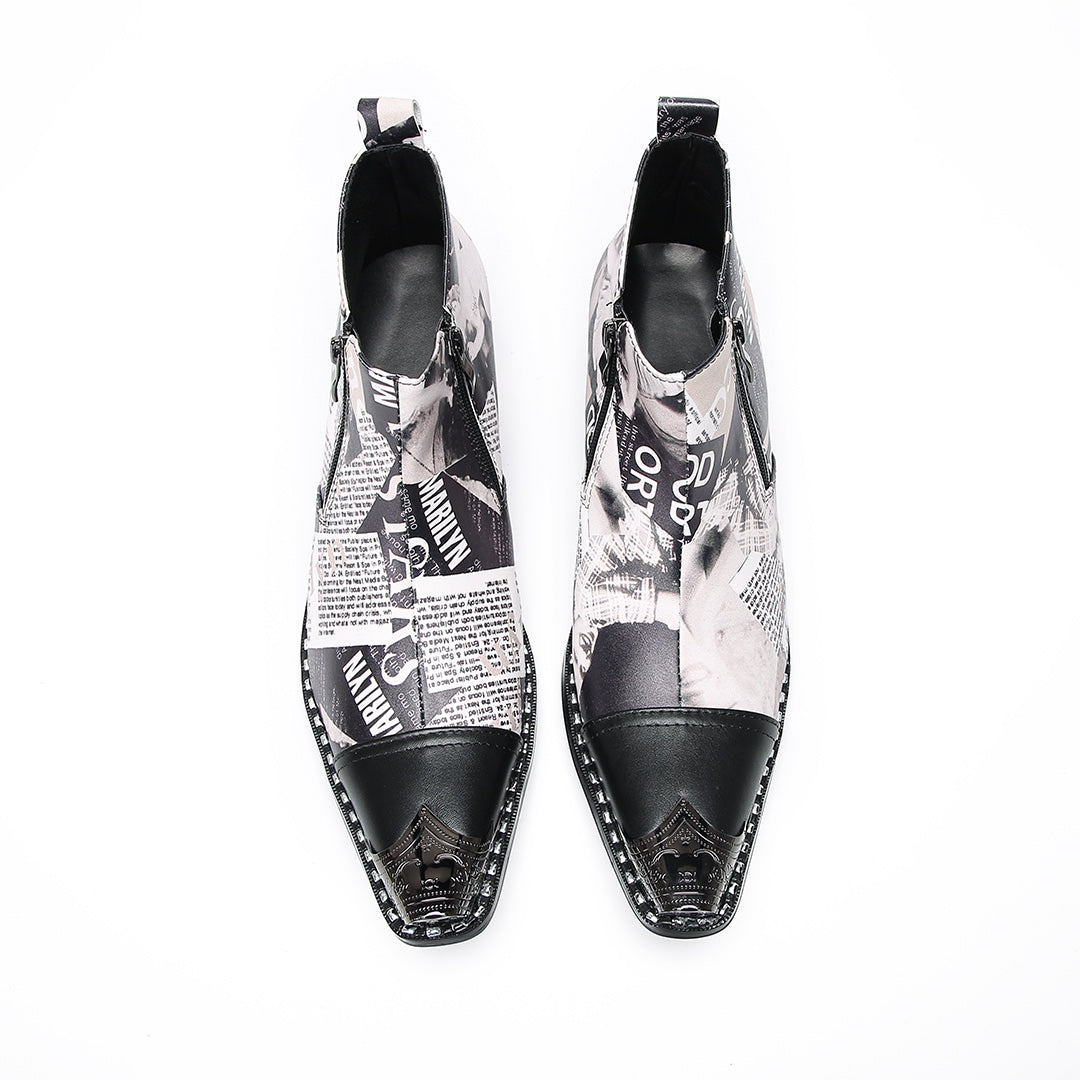 A pair of men's black and white newspaper print ankle boots with a pointed metal toe, side zipper, and block heel.