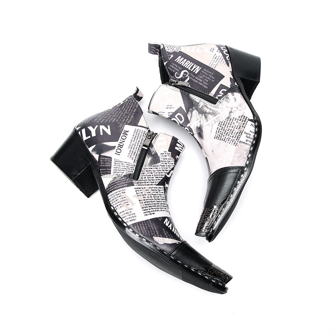 A pair of men's black and white newspaper print ankle boots with a pointed metal toe, side zipper, and block heel.