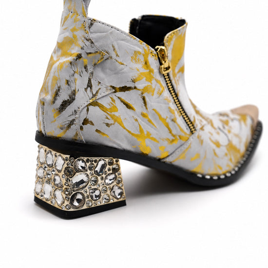 White and gold foil patterned ankle boot with a pointed metal toe, side zipper, and a block heel embellished with clear